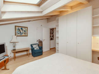 This charming bedroom features a unique architectural design with exposed wooden beams and a skylight, creating a bright and airy atmosphere.