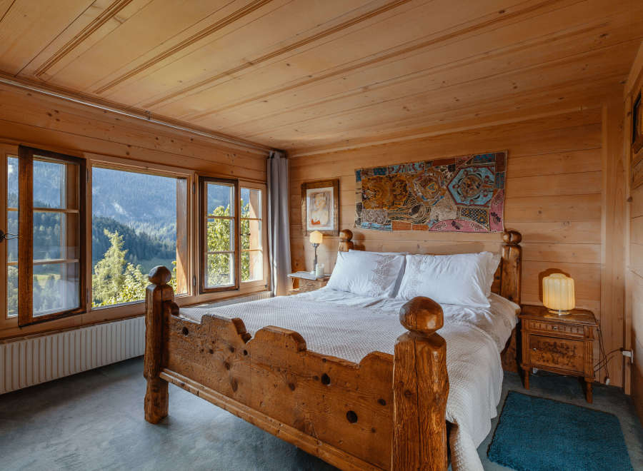 Experience the charm of this cozy bedroom, featuring rustic wooden walls and a stunning mountain view through the large windows.
