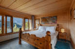 Experience the charm of this cozy bedroom, featuring rustic wooden walls and a stunning mountain view through the large windows.