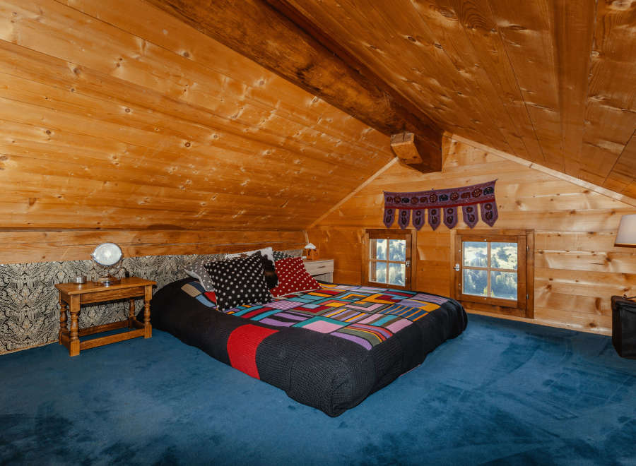 Cozy bedroom in a wooden cabin with a unique, colorful quilt.