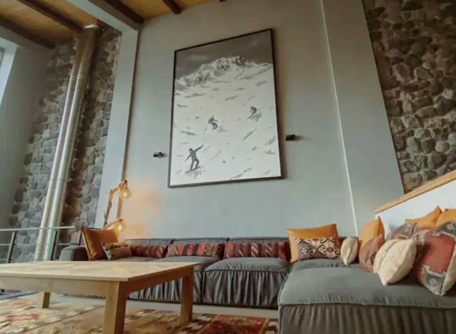 Experience the charm of this cozy living space, featuring a stunning mountain-themed artwork and a comfortable sectional sofa.