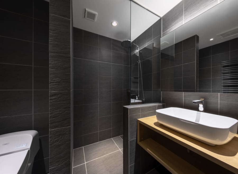 Modern bathroom with dark gray tiles, a glass shower enclosure, and a sleek wooden vanity with an integrated sink.