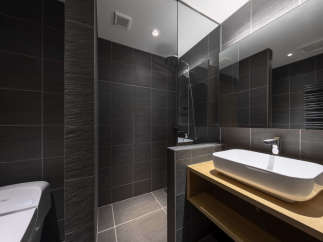 Modern bathroom with dark gray tiles, a glass shower enclosure, and a sleek wooden vanity with an integrated sink.