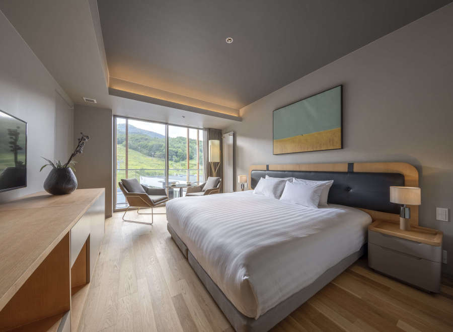 This hotel room boasts a king-size bed with crisp white linens, offering stunning mountain views from its large window.