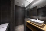 Modern bathroom with dark gray tiles, a glass shower enclosure, and a sleek wooden vanity with an integrated sink.