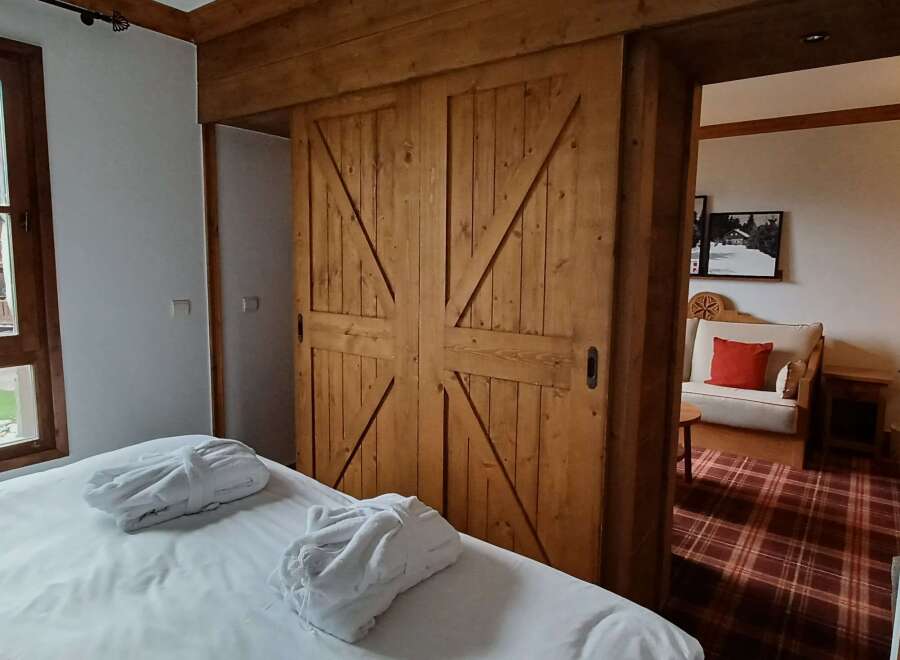 Experience rustic charm and modern comfort in this inviting bedroom, featuring a plush bed adorned with two white bathrobes, perfect for unwinding.
