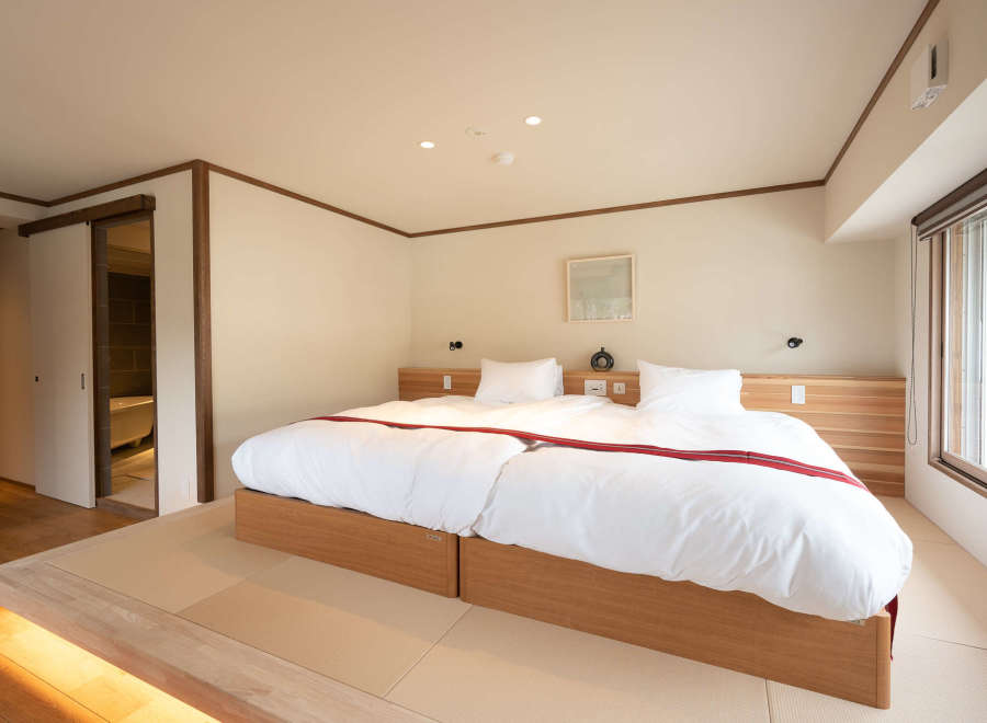 This serene bedroom features a minimalist design with a platform bed, tatami mats, and a sliding door leading to a modern bathroom.