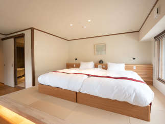 This serene bedroom features a minimalist design with a platform bed, tatami mats, and a sliding door leading to a modern bathroom.