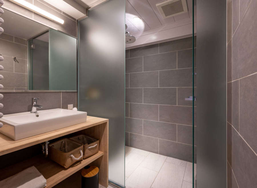 This modern bathroom boasts a sleek, minimalist design with gray tile, a frosted glass shower enclosure, and a floating wooden vanity with built-in storage.