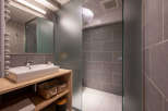 This modern bathroom boasts a sleek, minimalist design with gray tile, a frosted glass shower enclosure, and a floating wooden vanity with built-in storage.