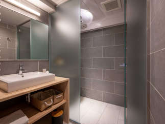 This modern bathroom boasts a sleek, minimalist design with gray tile, a frosted glass shower enclosure, and a floating wooden vanity with built-in storage.