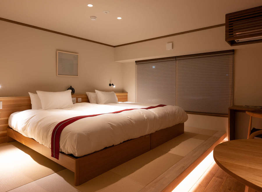Relax in this serene hotel room featuring a comfortable double bed with a wooden frame, complemented by soft lighting and tatami mats for a traditional Japanese touch.