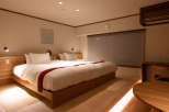Relax in this serene hotel room featuring a comfortable double bed with a wooden frame, complemented by soft lighting and tatami mats for a traditional Japanese touch.