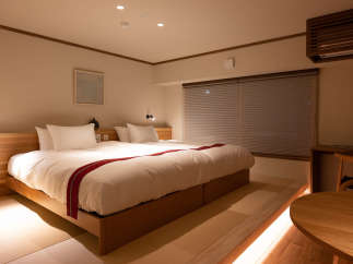 Relax in this serene hotel room featuring a comfortable double bed with a wooden frame, complemented by soft lighting and tatami mats for a traditional Japanese touch.