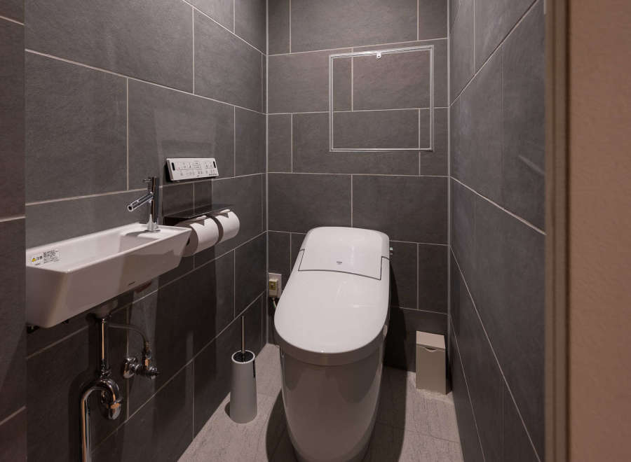 Modern bathroom with dark gray tile, wall-mounted sink and toilet, and sleek fixtures.