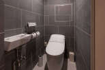 Modern bathroom with dark gray tile, wall-mounted sink and toilet, and sleek fixtures.