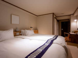 This cozy hotel room features a comfortable double bed with a stylish purple and silver patterned bed runner, perfect for a relaxing stay.