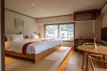 This modern hotel room features a comfortable double bed with a wooden frame, a tatami mat floor, and a large window offering stunning views of the surrounding cityscape.