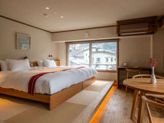 This modern hotel room features a comfortable double bed with a wooden frame, a tatami mat floor, and a large window offering stunning views of the surrounding cityscape.