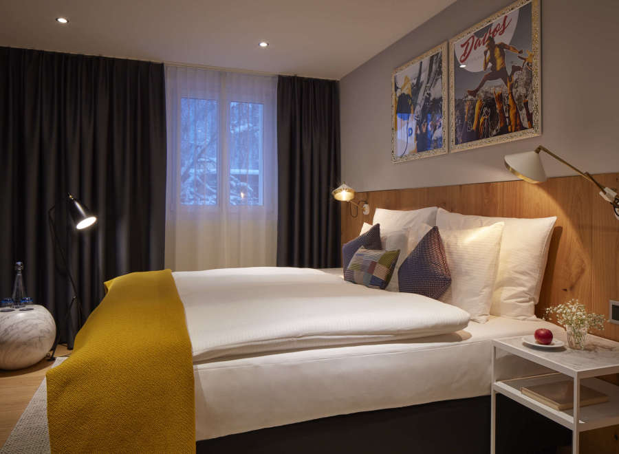 Cozy hotel room featuring a comfortable double bed with plush bedding and a warm yellow throw.