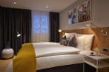 Cozy hotel room featuring a comfortable double bed with plush bedding and a warm yellow throw.