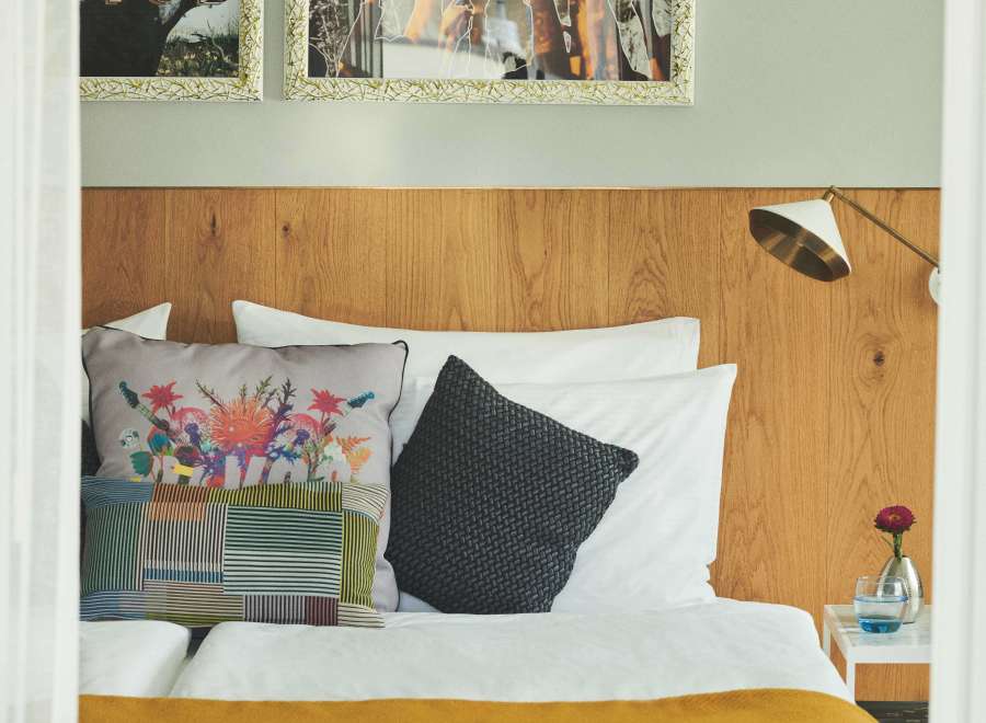 This cozy hotel room features a comfortable bed with a mustard yellow throw, complemented by patterned pillows and a dark gray accent pillow.