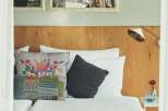 This cozy hotel room features a comfortable bed with a mustard yellow throw, complemented by patterned pillows and a dark gray accent pillow.