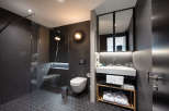 This modern bathroom boasts a sleek design with dark hexagon tiles, a glass shower enclosure, and a floating vanity with a wooden shelf for toiletries and towels.