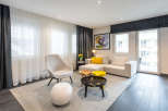Modern living room with light beige couch and armchair, complemented by dark gray curtains and flooring.
