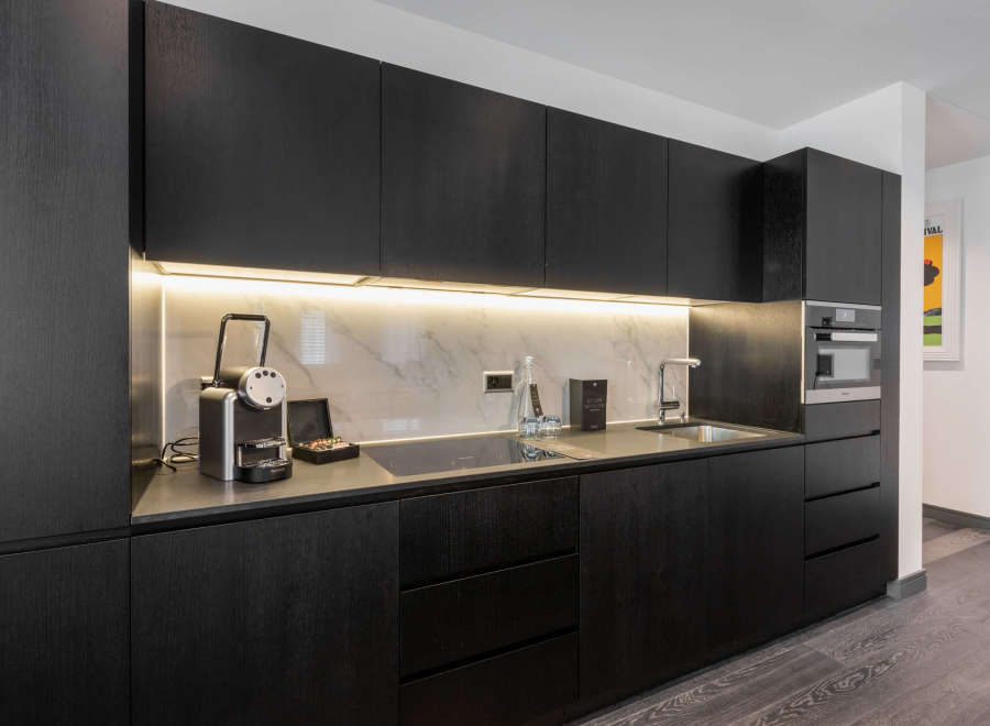 This modern kitchen boasts sleek black cabinetry, marble countertops, and integrated appliances, including a built-in oven and espresso machine.