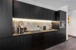 This modern kitchen boasts sleek black cabinetry, marble countertops, and integrated appliances, including a built-in oven and espresso machine.
