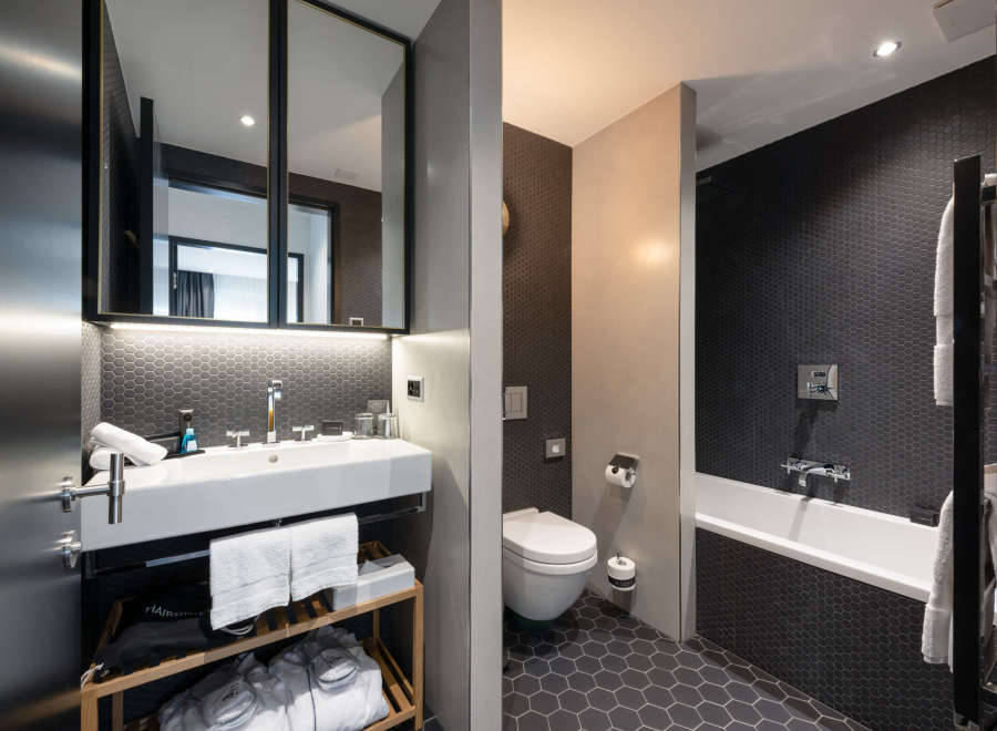 This modern bathroom boasts a sleek design with dark hexagon tiles, a white sink and toilet, and a freestanding bathtub.
