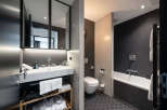 This modern bathroom boasts a sleek design with dark hexagon tiles, a white sink and toilet, and a freestanding bathtub.