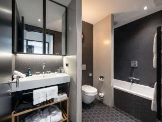This modern bathroom boasts a sleek design with dark hexagon tiles, a white sink and toilet, and a freestanding bathtub.