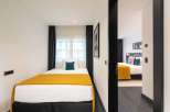 This modern apartment boasts two cozy bedrooms, each featuring a comfortable double bed dressed in crisp white linens and a warm mustard-yellow throw.