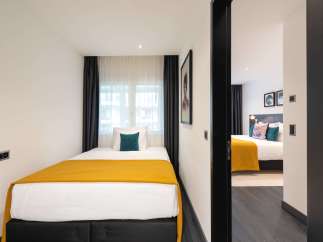 This modern apartment boasts two cozy bedrooms, each featuring a comfortable double bed dressed in crisp white linens and a warm mustard-yellow throw.