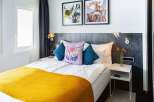Stylish hotel room featuring a comfortable double bed with a mustard yellow throw, complemented by teal and floral patterned pillows.