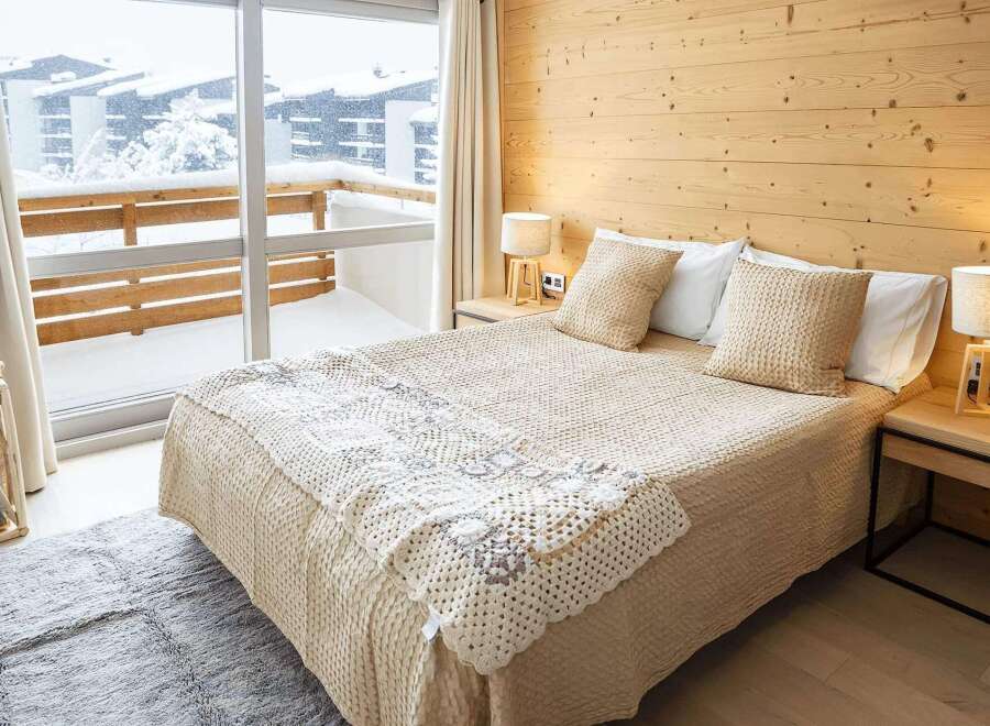 Cozy bedroom with a wooden wall and a view of a snowy landscape.