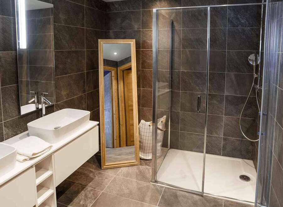 Modern bathroom with double sinks, a large walk-in shower, and stylish dark tile.