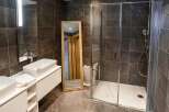 Modern bathroom with double sinks, a large walk-in shower, and stylish dark tile.