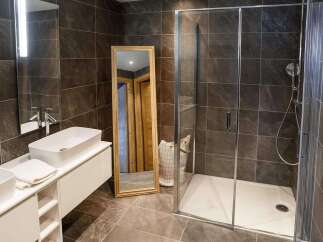 Modern bathroom with double sinks, a large walk-in shower, and stylish dark tile.