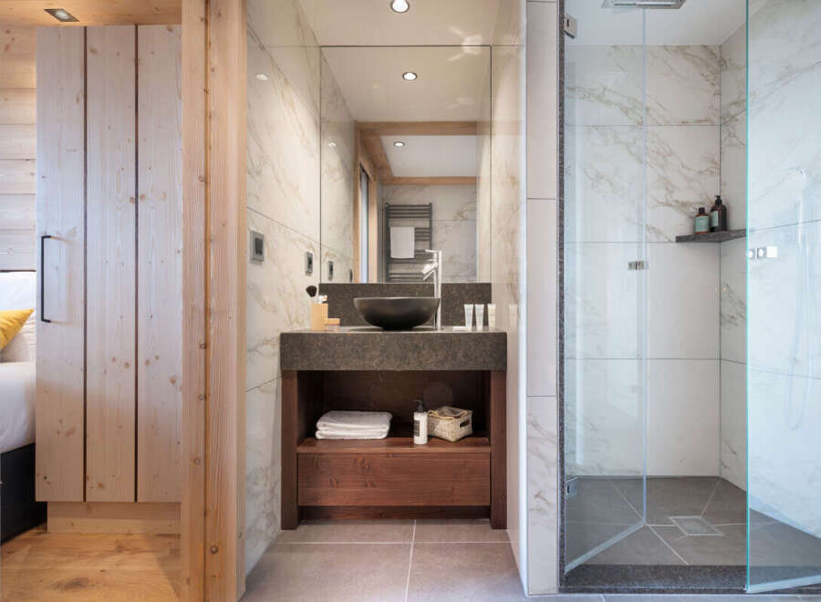 This stunning bathroom boasts a spacious walk-in shower with marble tiling, a sleek vanity with dark countertop and wooden cabinetry, and a large mirror reflecting the bright and airy space.