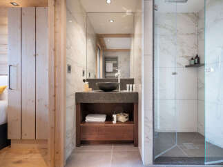 This stunning bathroom boasts a spacious walk-in shower with marble tiling, a sleek vanity with dark countertop and wooden cabinetry, and a large mirror reflecting the bright and airy space.