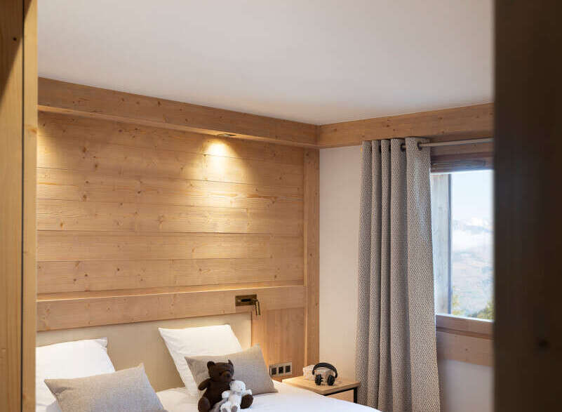 Cozy twin bedroom with wooden walls and beams, featuring plush bedding and a playful atmosphere with children's toys and games.
