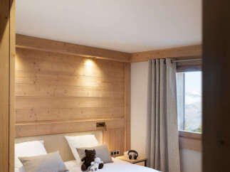 Cozy twin bedroom with wooden walls and beams, featuring plush bedding and a playful atmosphere with children's toys and games.