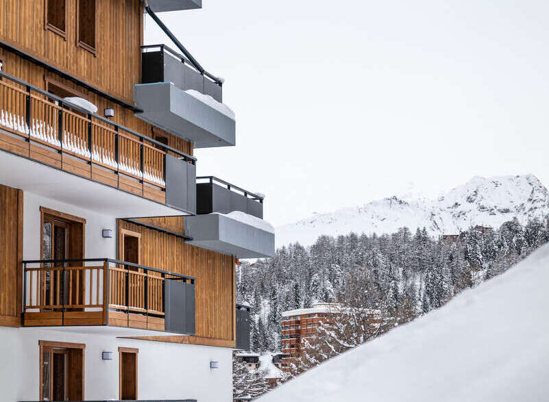 This stunning chalet boasts modern architecture with a blend of wood and gray accents, offering breathtaking views of snow-capped mountains.