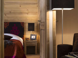 This cozy bedroom features a rustic wooden wall, a comfortable bed with a rich colored quilt, and a bedside table with a lamp.