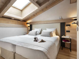 Cozy attic bedroom with wooden beams and skylights, featuring a double bed with plush bedding and a sheep toy.