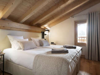 Cozy chalet bedroom with wooden beams, plush bedding, and a view of the snowy landscape.