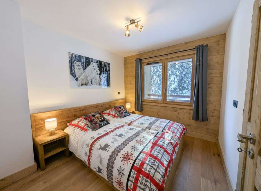 Cozy bedroom with wooden walls and floors, featuring a double bed with festive bedding and a large window offering stunning views of a snow-covered landscape.